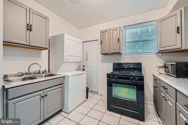 kitchen featuring stainless steel microwave, stacked washer / drying machine, black range with gas stovetop, gray cabinets, and light countertops