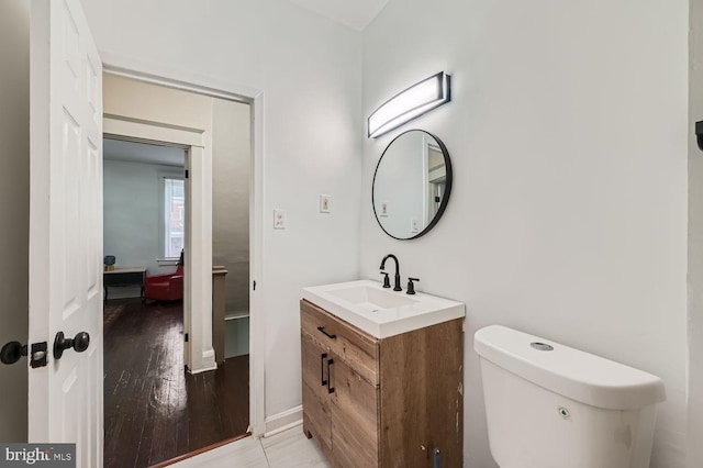 half bath with toilet, wood finished floors, and vanity