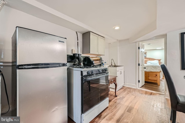 kitchen featuring baseboards, light wood-style flooring, freestanding refrigerator, gas range gas stove, and a sink