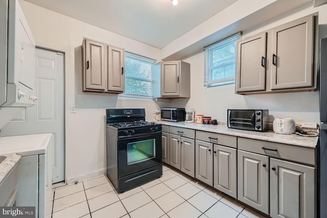 kitchen with a toaster, stainless steel microwave, black gas range oven, light tile patterned flooring, and baseboards