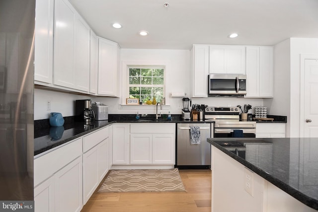 kitchen featuring stainless steel appliances, dark stone counters, white cabinetry, and light hardwood / wood-style flooring