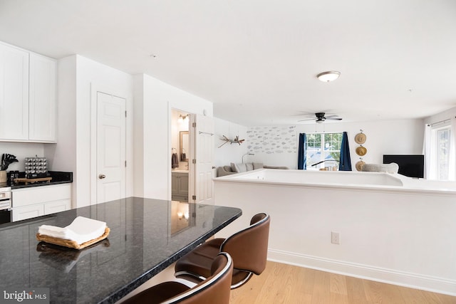 kitchen with dark stone counters, light wood-type flooring, ceiling fan, a breakfast bar area, and white cabinetry