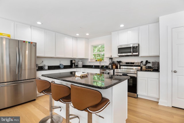 kitchen with appliances with stainless steel finishes, light wood-type flooring, a center island, and a kitchen breakfast bar