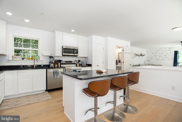 kitchen with light hardwood / wood-style floors, white cabinets, a kitchen island, stainless steel appliances, and sink