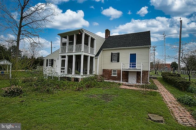 back of property featuring a balcony, a sunroom, and a lawn