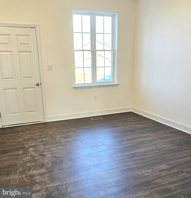 unfurnished room featuring dark wood-type flooring, visible vents, and baseboards