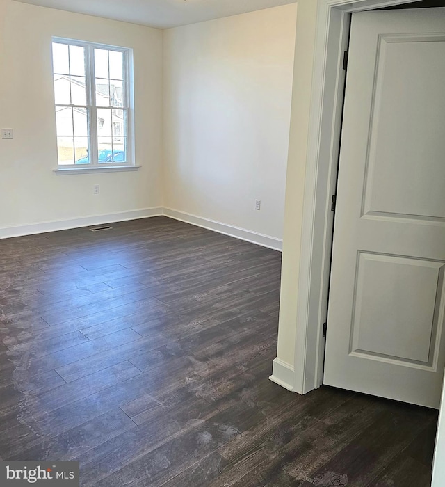 unfurnished room with baseboards, visible vents, and dark wood finished floors