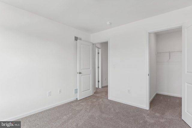 unfurnished bedroom featuring a spacious closet, carpet, visible vents, and baseboards