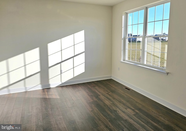 unfurnished room with dark wood-style floors, visible vents, and baseboards