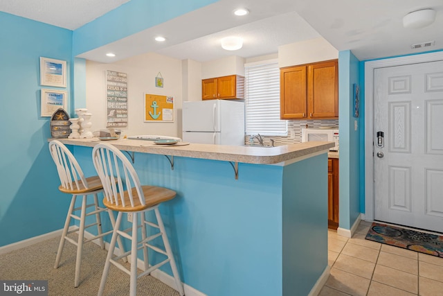 kitchen with kitchen peninsula, light tile patterned floors, a kitchen breakfast bar, backsplash, and white refrigerator