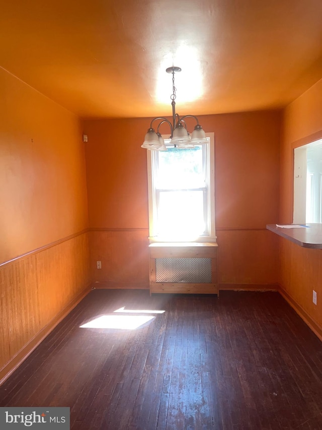 empty room featuring radiator heating unit, dark hardwood / wood-style flooring, and a chandelier