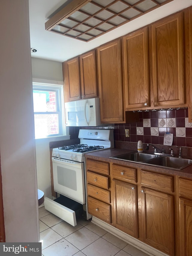 kitchen featuring backsplash, white appliances, sink, and light tile floors