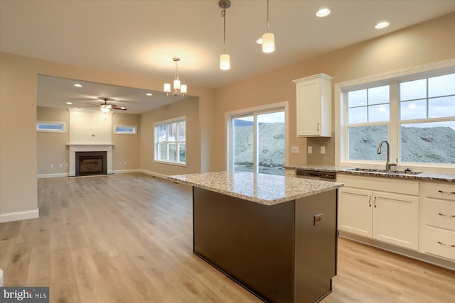 kitchen featuring light wood-type flooring, a fireplace with flush hearth, light stone counters, and a sink