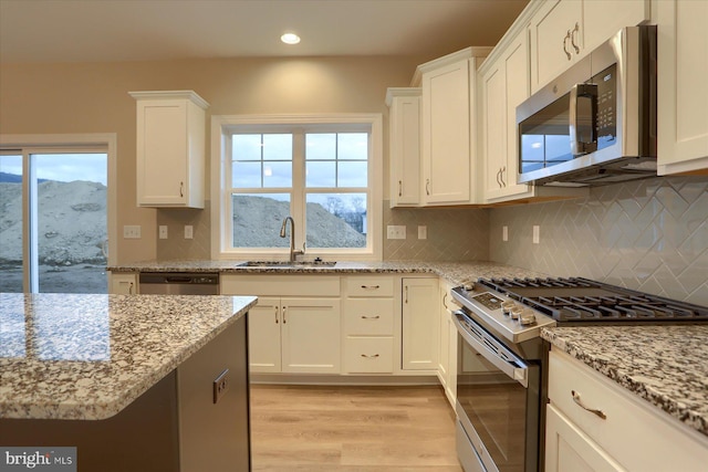 kitchen featuring appliances with stainless steel finishes, a sink, light wood-style flooring, and white cabinets