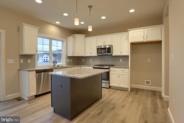 kitchen with appliances with stainless steel finishes, white cabinetry, a sink, a kitchen island, and light wood-type flooring