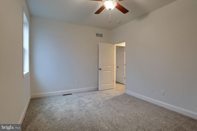 spare room with baseboards, visible vents, a ceiling fan, and light colored carpet