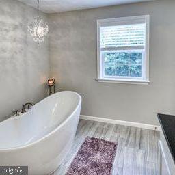 bathroom featuring wood-type flooring, vanity, an inviting chandelier, and a bathing tub