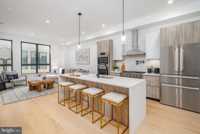 kitchen with hanging light fixtures, appliances with stainless steel finishes, light wood-type flooring, wall chimney range hood, and a breakfast bar area