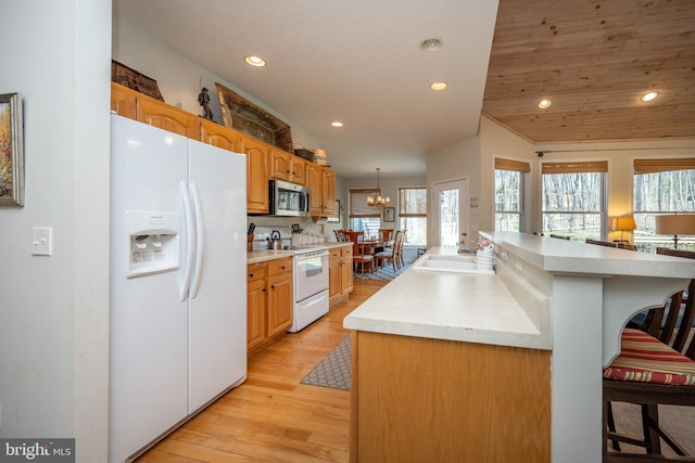 kitchen featuring white appliances, sink, lofted ceiling, a breakfast bar area, and light wood-type flooring