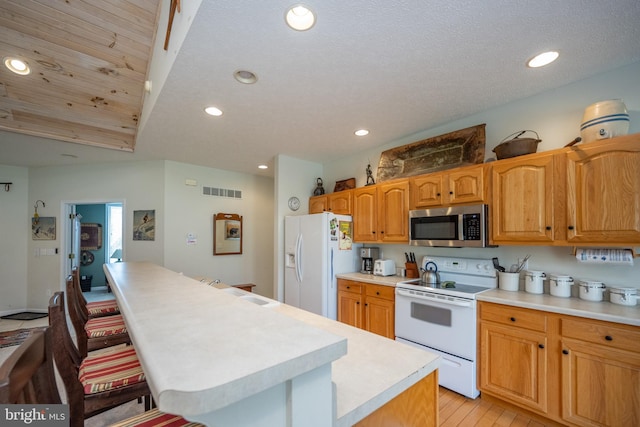 kitchen with a center island, a kitchen bar, a textured ceiling, light hardwood / wood-style flooring, and white appliances