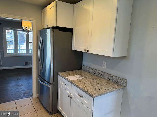 kitchen featuring light tile floors, light stone countertops, white cabinetry, and stainless steel fridge