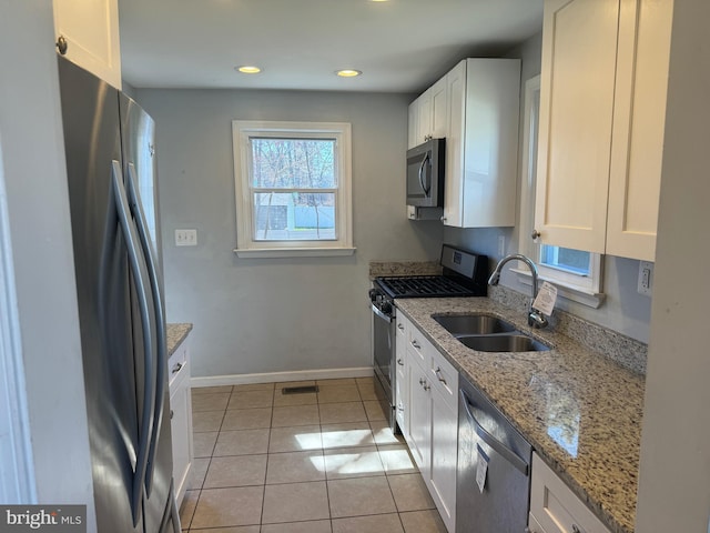 kitchen featuring sink, appliances with stainless steel finishes, light tile flooring, light stone countertops, and white cabinetry