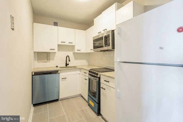 kitchen with appliances with stainless steel finishes, sink, light tile floors, white cabinets, and tasteful backsplash