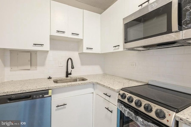 kitchen with tasteful backsplash, light stone counters, stainless steel appliances, sink, and white cabinetry