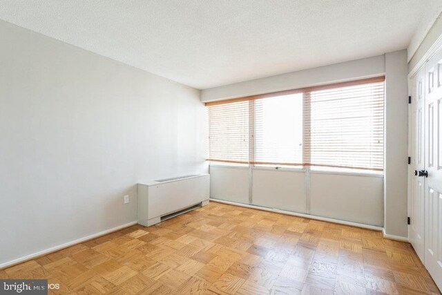 spare room with radiator heating unit, a textured ceiling, and light parquet flooring