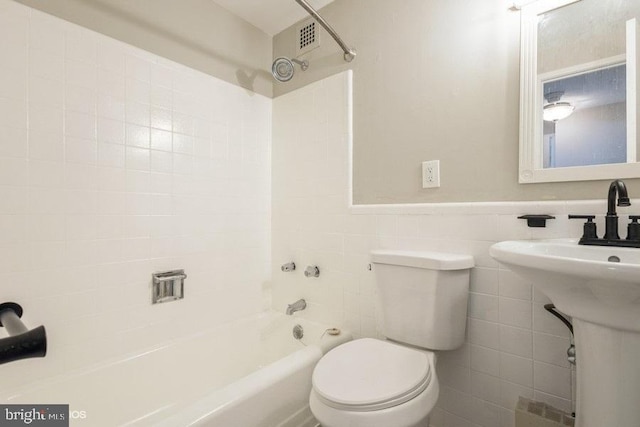 bathroom with tiled shower / bath combo, tile walls, and toilet