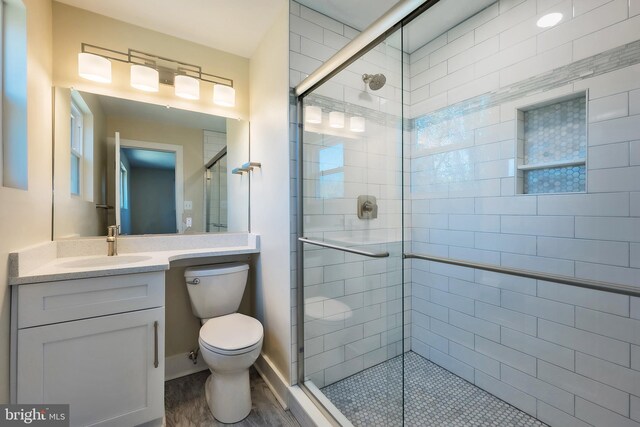 bathroom with wood-type flooring, a shower with shower door, vanity with extensive cabinet space, and toilet