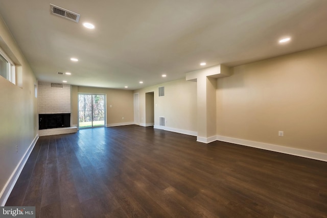 unfurnished living room with brick wall, dark wood-type flooring, and a brick fireplace