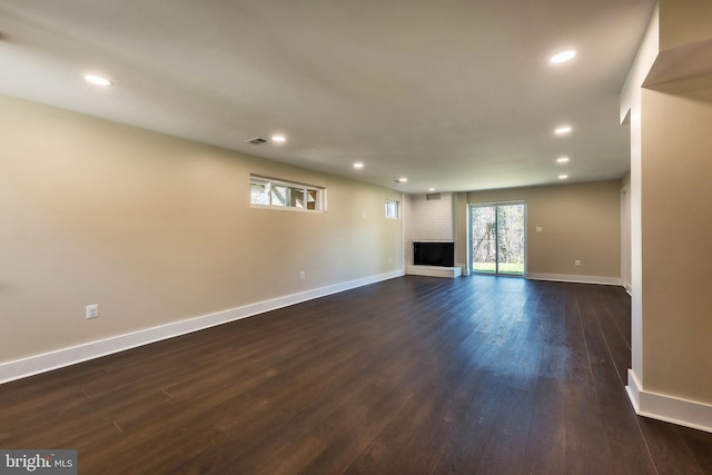 unfurnished living room with dark hardwood / wood-style flooring and a brick fireplace