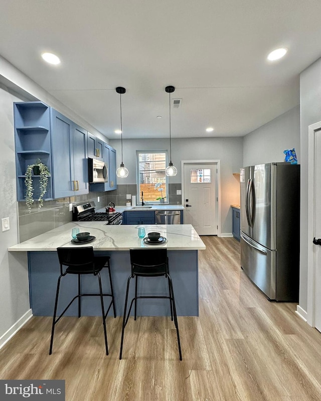 kitchen with kitchen peninsula, stainless steel appliances, light hardwood / wood-style floors, pendant lighting, and a breakfast bar