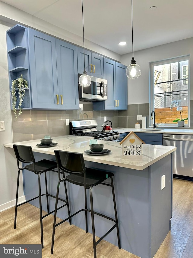 kitchen with appliances with stainless steel finishes, backsplash, light hardwood / wood-style floors, a kitchen breakfast bar, and pendant lighting