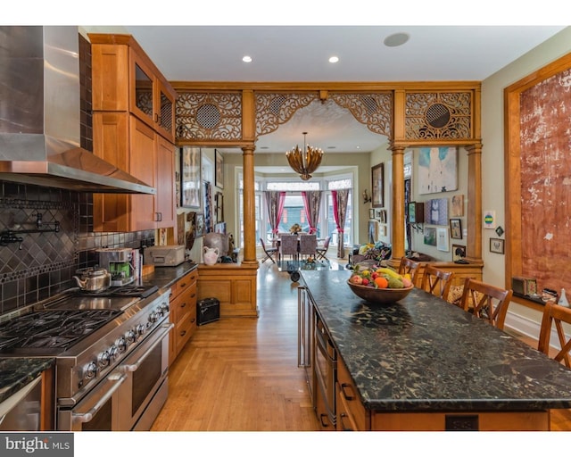 kitchen featuring double oven range, ornate columns, wall chimney range hood, light parquet flooring, and tasteful backsplash