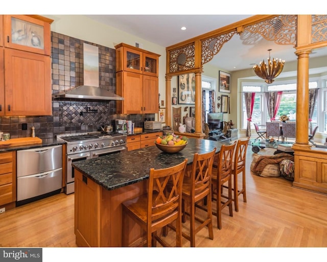 kitchen featuring a notable chandelier, a breakfast bar, wall chimney exhaust hood, range with two ovens, and decorative columns