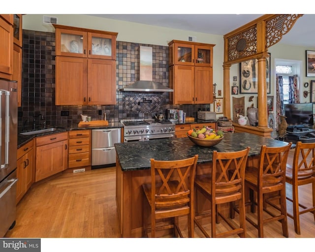 kitchen featuring backsplash, a breakfast bar, sink, high end appliances, and wall chimney range hood