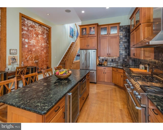 kitchen with a kitchen island, high end appliances, light hardwood / wood-style floors, wall chimney exhaust hood, and tasteful backsplash