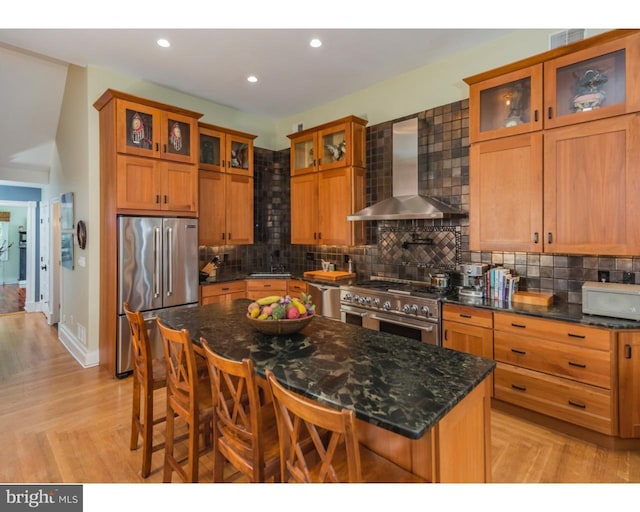 kitchen with a kitchen breakfast bar, a kitchen island, wall chimney range hood, high end appliances, and backsplash