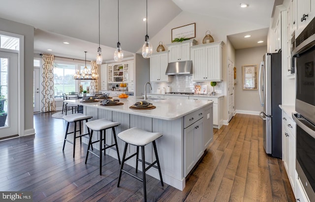 kitchen featuring pendant lighting, a center island with sink, dark wood-type flooring, white cabinets, and backsplash