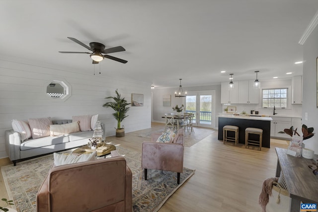 living room with ornamental molding, light hardwood / wood-style flooring, and ceiling fan with notable chandelier