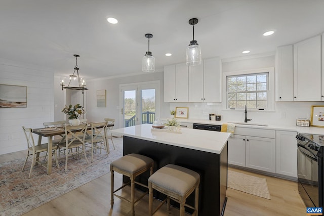 kitchen with hanging light fixtures, light hardwood / wood-style floors, black appliances, and sink