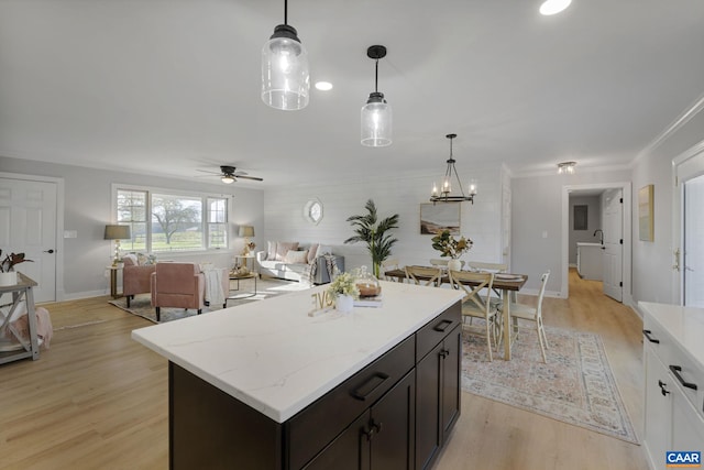 kitchen with pendant lighting, a kitchen island, light stone countertops, ceiling fan with notable chandelier, and light wood-type flooring