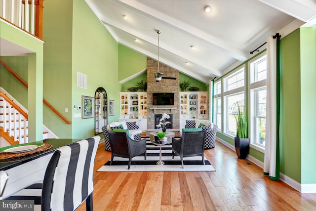 living room featuring light wood-type flooring, beamed ceiling, a fireplace, brick wall, and high vaulted ceiling