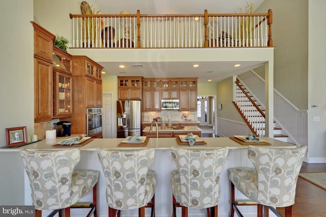 kitchen with a high ceiling, hardwood / wood-style floors, backsplash, appliances with stainless steel finishes, and a breakfast bar