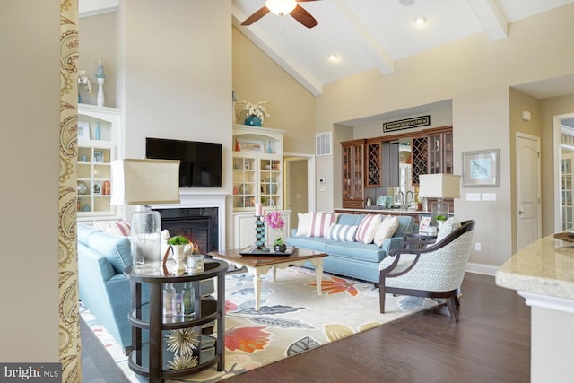 living room featuring high vaulted ceiling, ceiling fan, beamed ceiling, a tiled fireplace, and dark hardwood / wood-style flooring