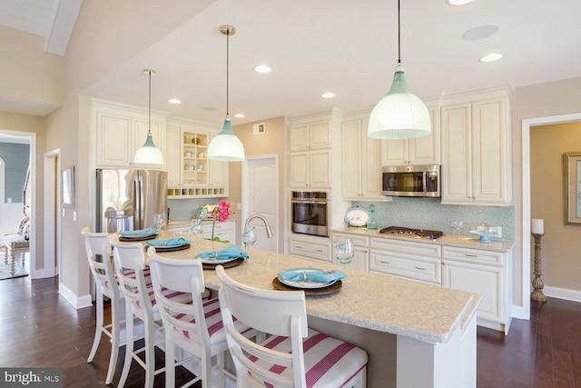 kitchen featuring an island with sink, dark hardwood / wood-style flooring, appliances with stainless steel finishes, tasteful backsplash, and a kitchen bar