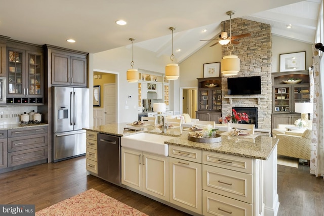 kitchen with dark wood-type flooring, light stone counters, a stone fireplace, stainless steel appliances, and ceiling fan