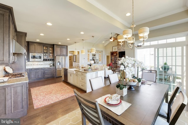 dining area with ceiling fan with notable chandelier, sink, light wood-type flooring, vaulted ceiling, and crown molding